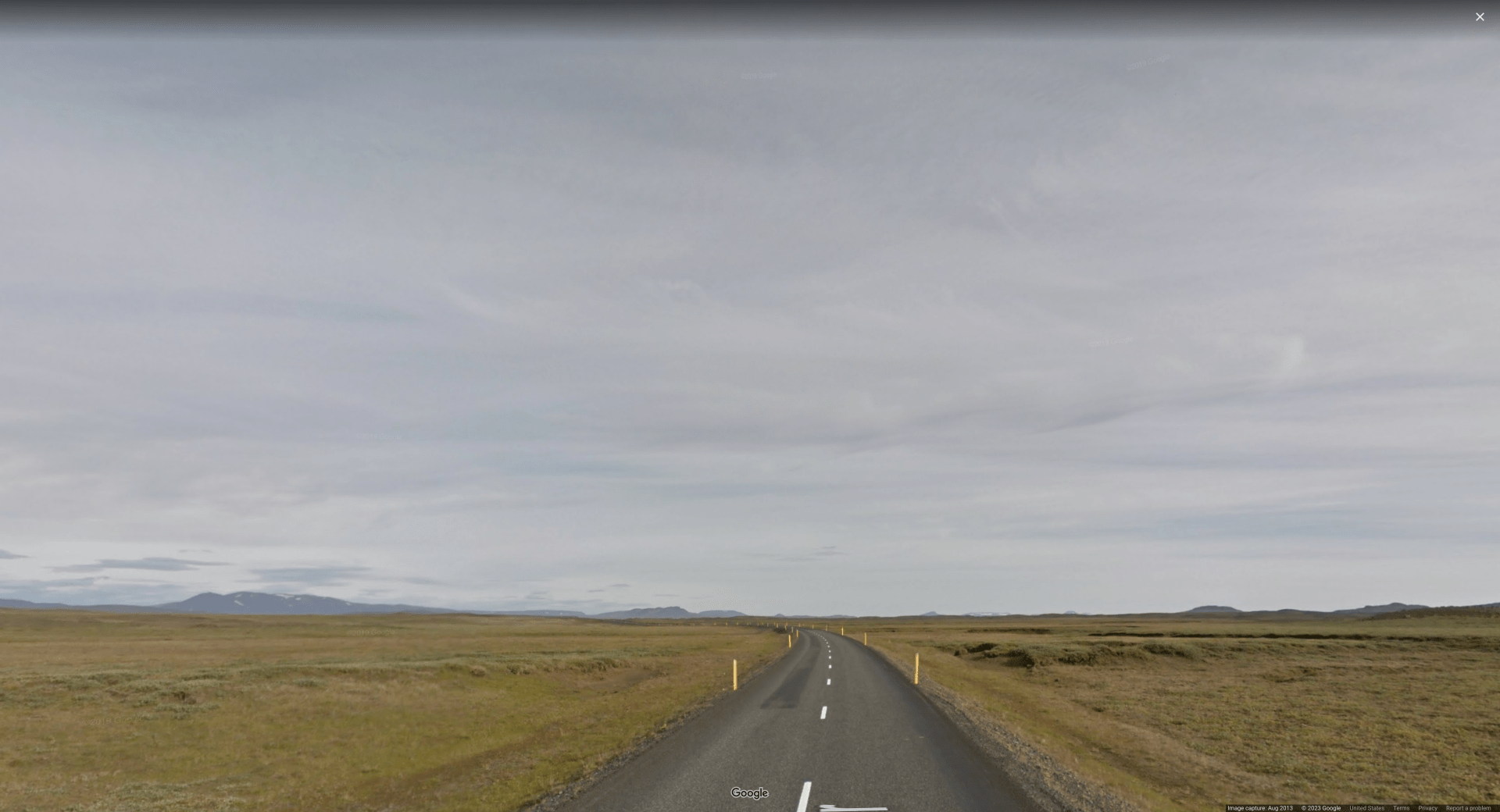 Picture of a road in an extremely flat & empty plains, with overcast skies and yellow reflector poles