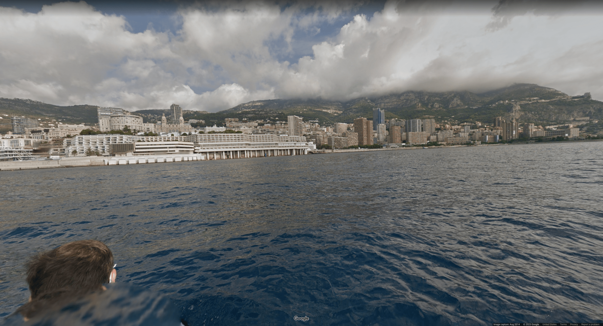 Picture taken in the water off the shore of a large city’s downtown area. The buildings are mostly white and there are hills in the background